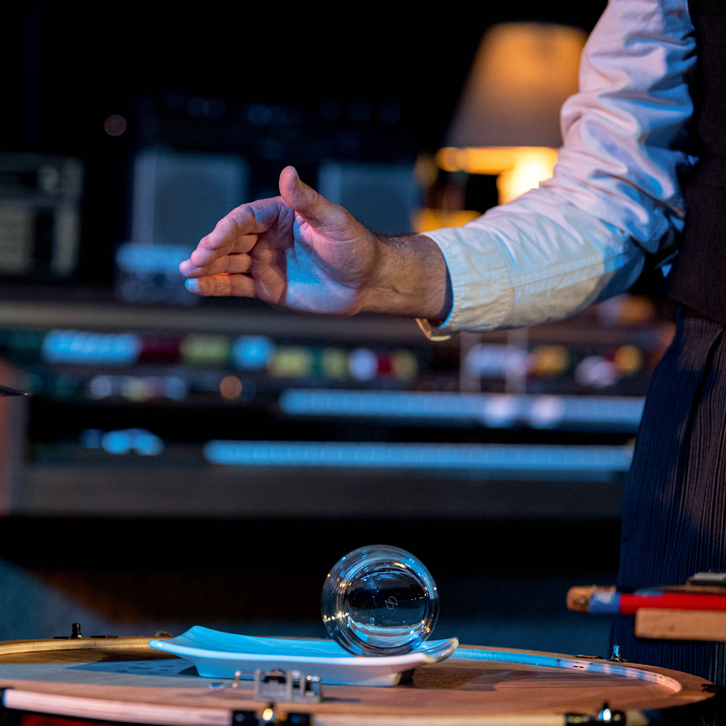 Musician's hands shown after releasing a rolling glass on a curved plate in performance